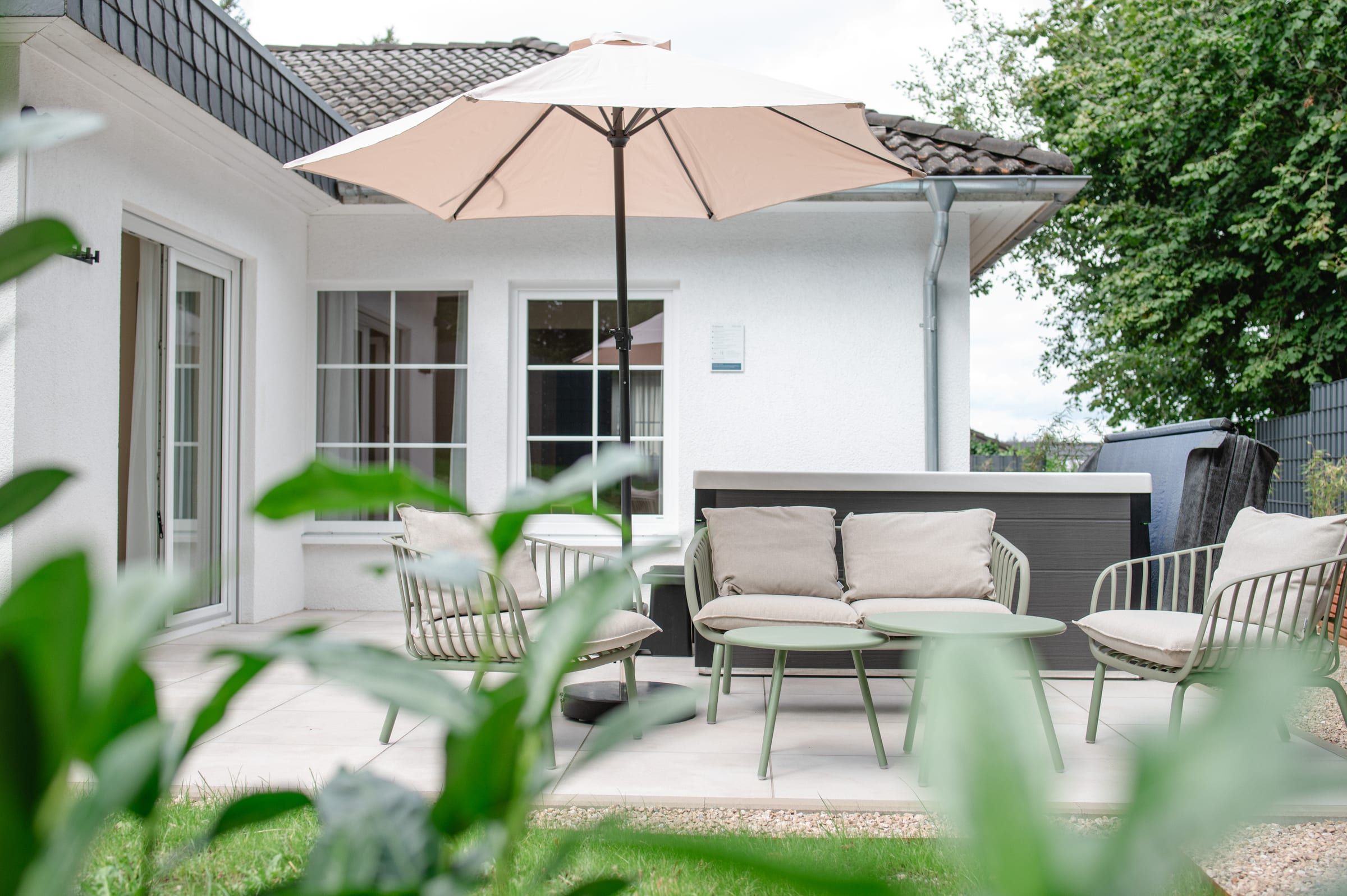 Terrasse mit Loungemöbeln, Sonnenschirm und Whirlpool, im Vordergrund Grün